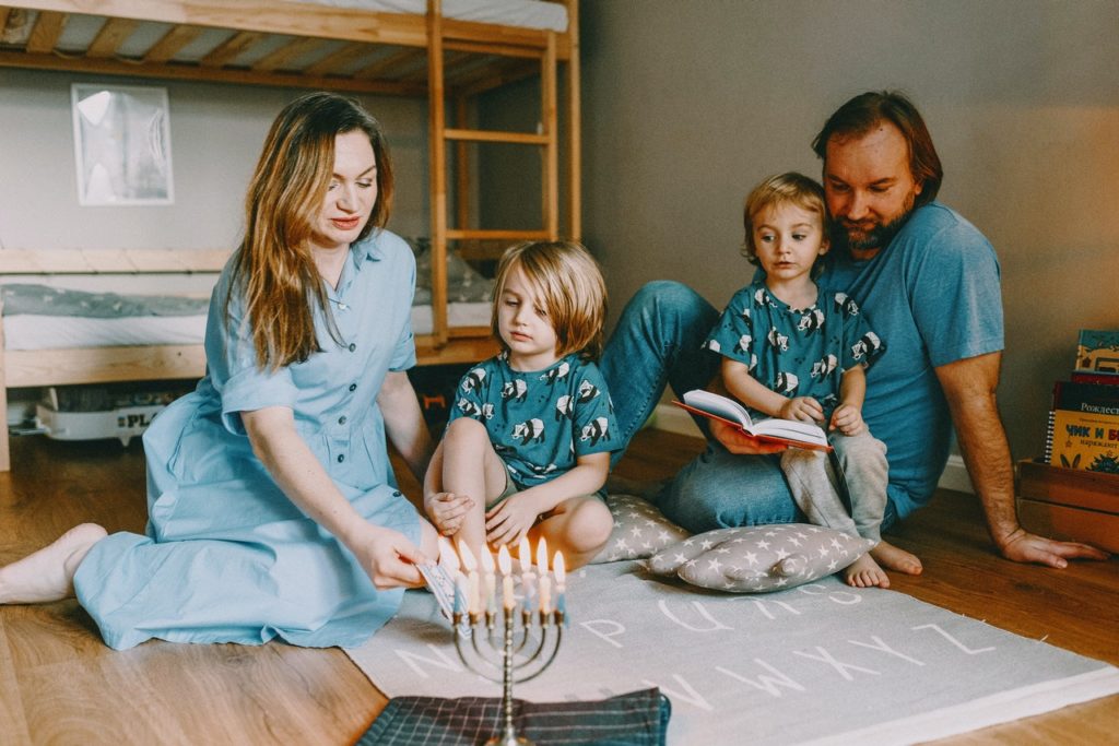 הורים ושני ילדים מדליקים נרות חנוכה על הרצפה